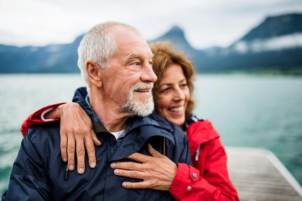 Senior couple tourist standing by lake in nature on holiday, hugging. 