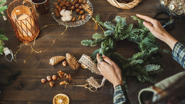 Beautiful woman making Christmas wreath using fresh pine branches and festive decorations. 