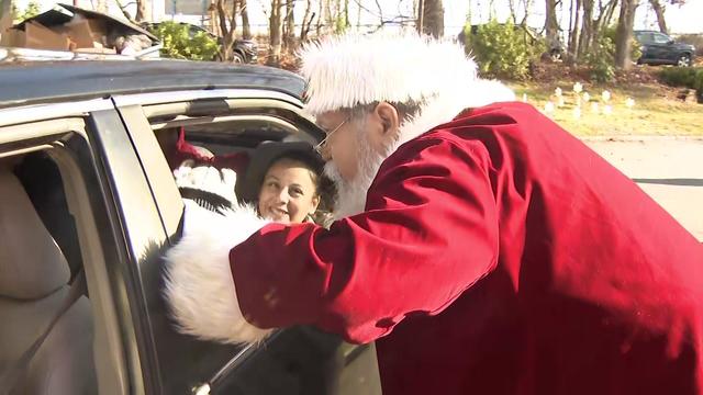 Santa Claus leans in a car window to talk to a child. 