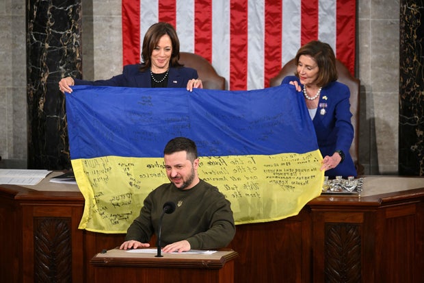 Ukrainian President Volodymyr Zelenskyy addresses Congress as Vice President Kamala Harris and House Speaker Nancy Pelosi hold a Ukrainian national flag that Zelensky gave them at the U.S. Capitol on Dec. 21, 2022.
