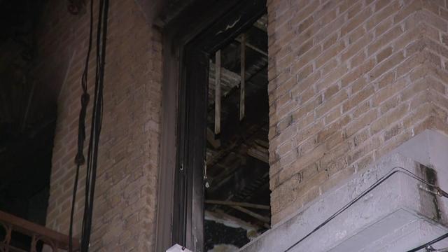 The fire-damaged interior of a building can be seen through a broken window. 