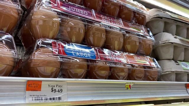 Cartons of eggs sit on the shelf in a grocery store. The price tag is $9.49. 