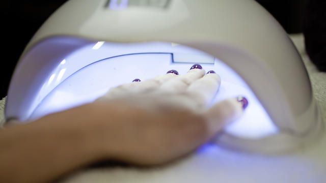 Woman Fliling Nails With UV Lamp in Background. 