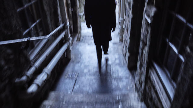 Man with black coat walking down a narrow alley, footpath, thoroughfare from the Royal Mile, Edinburgh 