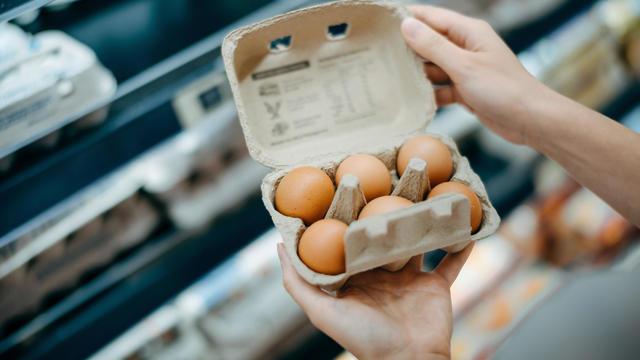 Close up of young Asian woman grocery shopping in a supermarket. She is holding a box of fresh organic free range eggs in front of a refrigerated section. Healthy eating lifestyle 