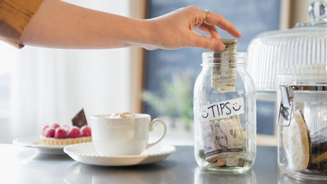 Hand putting money in tip jar on coffee shop counter 