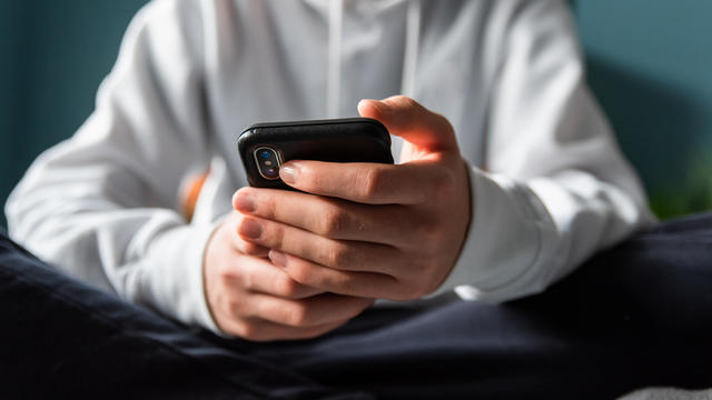 Close up of hands of teen boy in white sweater texting on phone. 