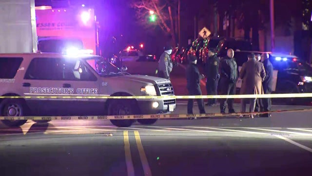 Law enforcement vehicles and officers stand behind crime scene tape at an intersection. 