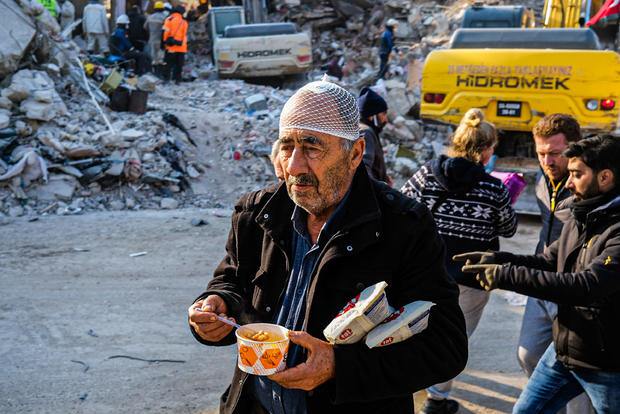An injured earthquake survivor walks as he eats near the 