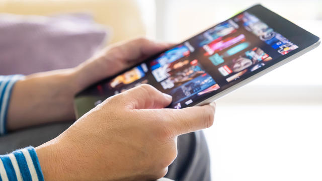 Selective focus at men hand and digital tablet. Young Adult Asian man holding tablet device while choose online movie streaming application with mobile wireless network at home. Entertainment concept. 