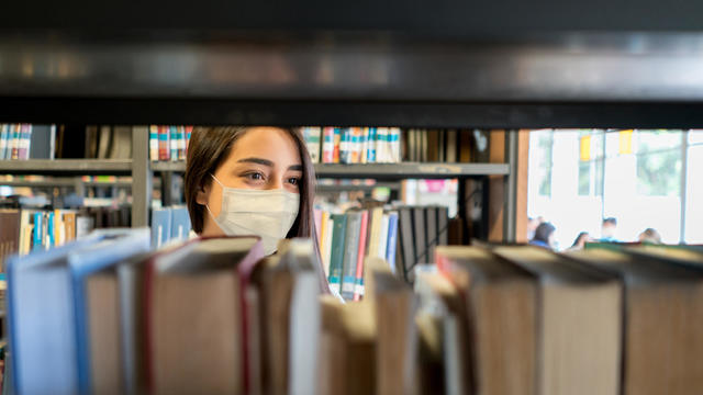 Student wearing a facemask at the library while looking for a book 