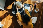 Overhead view of young Asian woman sitting on the floor in her bedroom, packing a suitcase for a trip. Getting ready for a vacation. Traveller's accessories. Travel and vacation concept 
