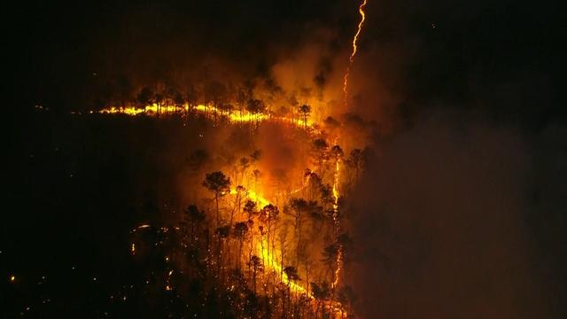 An aerial shot of smoke pouring from a wooded area. 