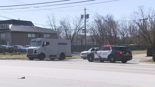 A police vehicle sits parked near an armored Brinks truck. 