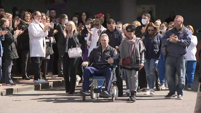 FDNY Lt. Bill Doody leaves a hospital in a wheelchair, surrounded by medical staff and others applauding. 