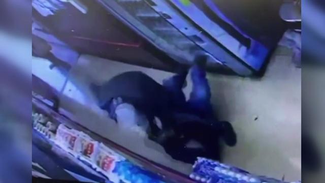 Surveillance video shows an individual standing over a man who is lying on the ground in a grocery store. 