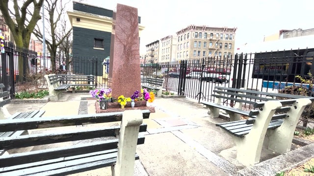 Flowers sit at the bottom of a granite memorial surrounded by benches. 