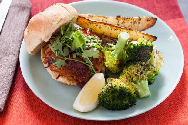 Plated BBQ tempeh sandwiches with roasted potato wedges & broccoli on red tablecloth