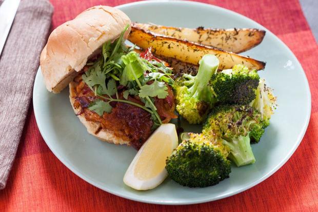 Plated BBQ tempeh sandwiches with roasted potato wedges & broccoli on red tablecloth 