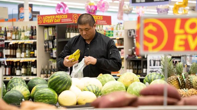 Asian man bags bananas in produce aisle 