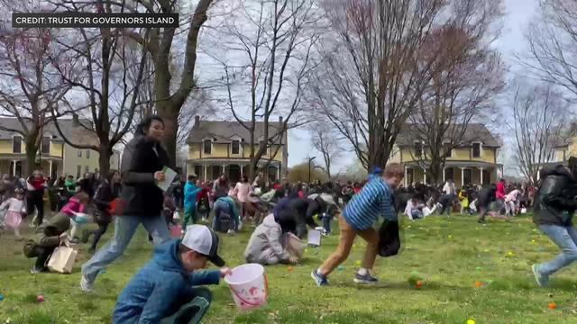 Dozens of children and adults pick up painted Easter eggs in a grassy field. 