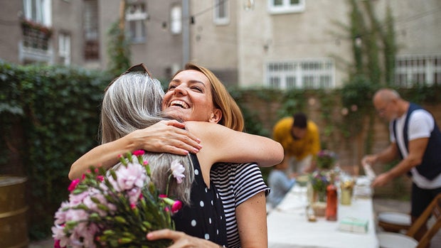 Happy adult daughter with bouquet hugging her senior mother outdoors in garden 