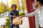 Male courier with bicycle delivering fast food to the customer in city. 