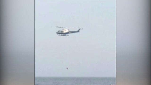 A helicopter lowers a basket to the water off Coney Island Pier. 