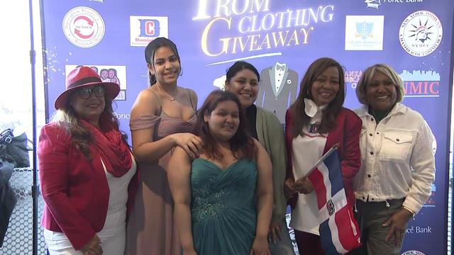 Four women pose with two students in prom dresses. 