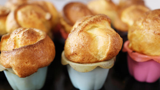 Homemade popover, which is a lush, airy and egg hollow roll, fresh from the oven. Yorkshire pudding freshly baked in silicone blue and pink baking dishes, selective focus 