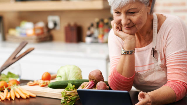 Woman leaning over tablet next to fresh food on kitchen counter 