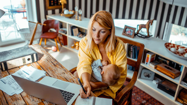 Young mother breastfeeding while working from home 