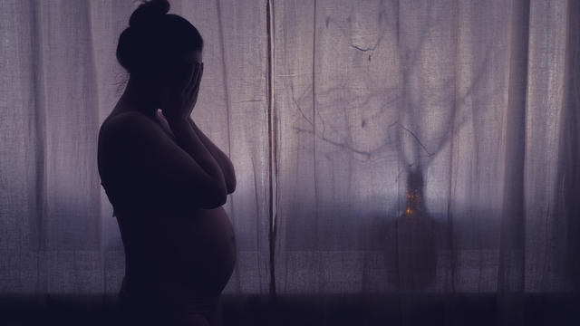 Young pregnant woman crying with her hands folded near her face. Pregnancy problems, silhouette of the expectant mother at the night window 
