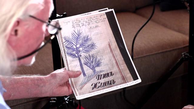 Peter Mathews looks at a photocopy of a page from a diary with a drawing of trees and Vietnamese writing on it. 