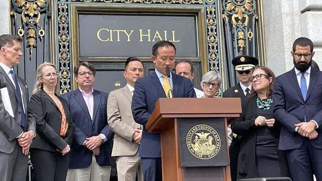 David Chiu stands at a podium in front of City Hall 