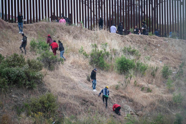 Asylum seekers are seen scaling a hill between the US-Mexico