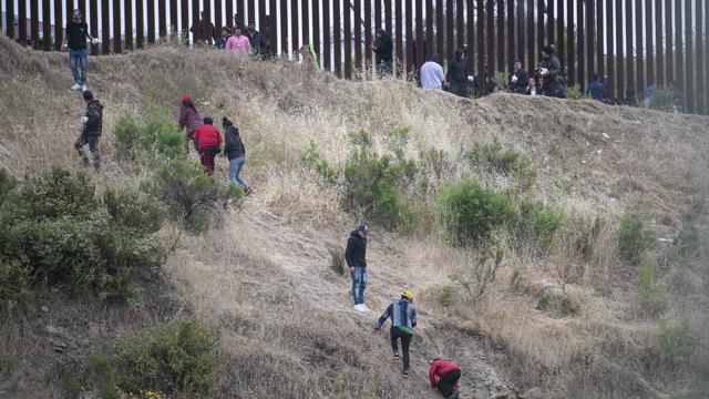 Asylum seekers are seen scaling a hill between the US-Mexico 