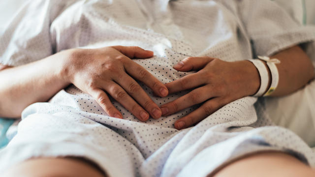 Young woman hospitalized in a bed. Gesture of pain in her belly. 