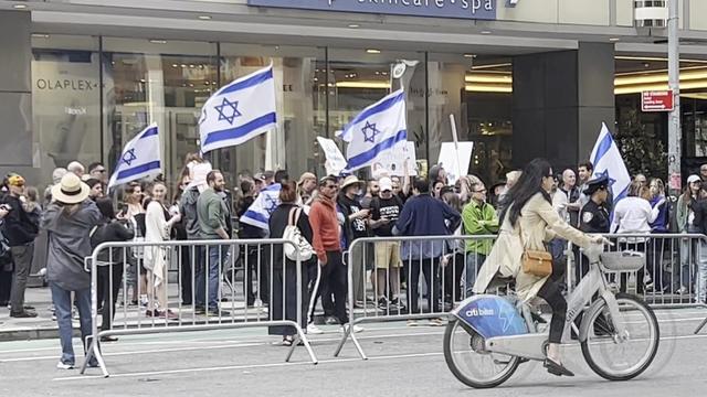 Paradegoers, some holding the flag of Israel, line up along a New York City street. 
