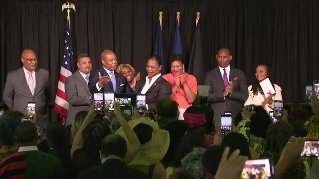 Mayor Eric Adams and NYPD Commissioner Keechant Sewell stand behind a podium along with others. 