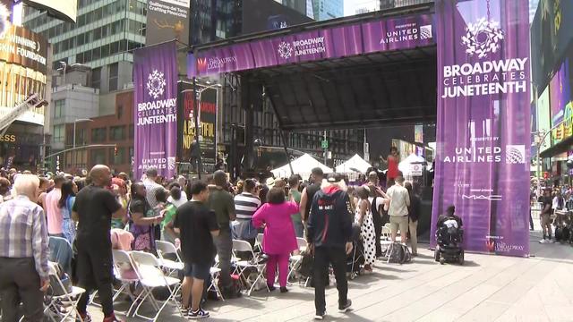 A crowd stands in front of a stage that has banners reading "Broadway Celebrates Juneteenth." 