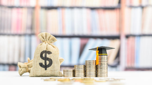 Tuition payment or tuition fee, expense for graduate study abroad program concept : Black graduation cap on stacks of coins, depicting fees charged by education institution for instruction or services 
