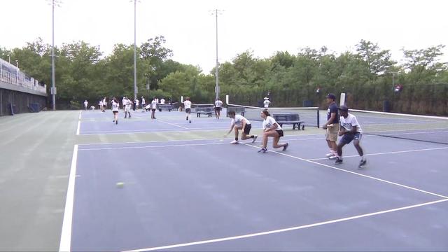 Dozens of people stand on tennis courts trying out to be ballpeople. 