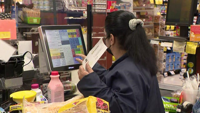 A cashier holds a grocery voucher while checking out customers 