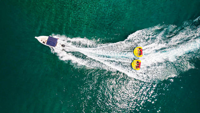 an inflatable tube attached to the boat, extreme water sports, water activity by boat, inflatable raft attached to the speedboat, people having fun in the water, aerial water sports, ringo and banana water sports 