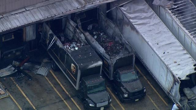 An aerial view of four tractor-trailers parked at a UPS warehouse. All four have suffered fire damage. 