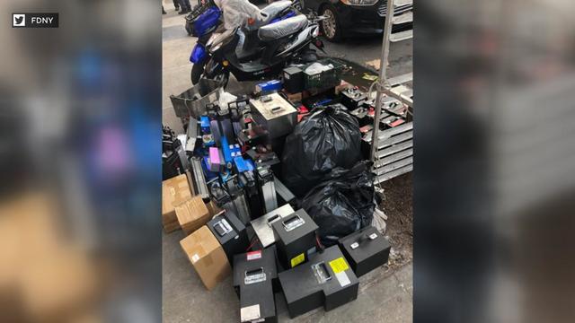 Dozens of lithium-ion batteries collected on a curb near several motorcycles. 