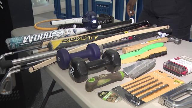 A number of items that are banned from planes displayed on a table, including: bats, golf clubs, tools, gardening equipment, kitchen knives and weights. 