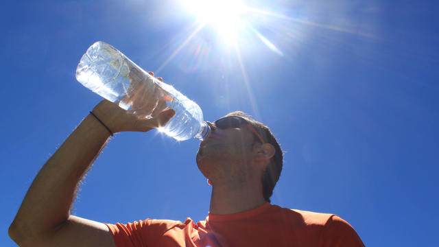 man drinking water with the sun over him 