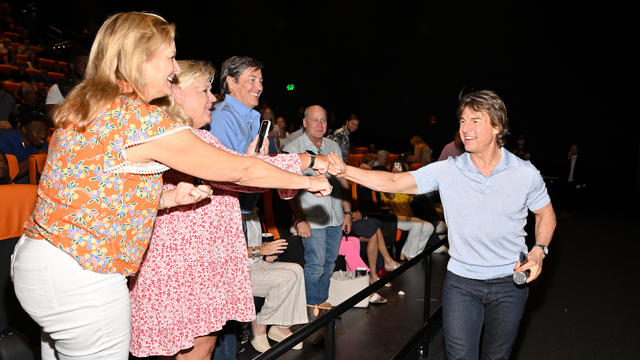 Tom Cruise gives fist bumps to audience members inside a movie theater. 